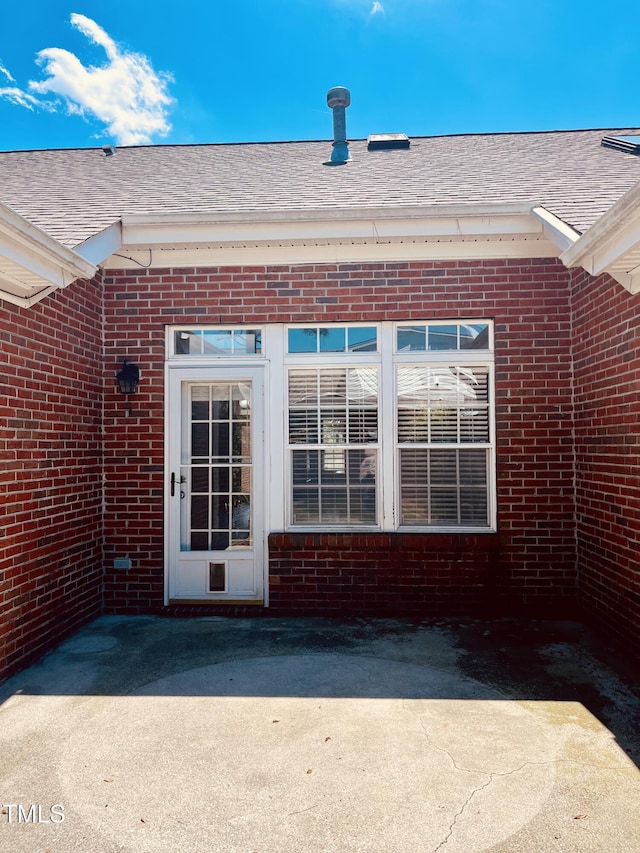 property entrance featuring brick siding and roof with shingles