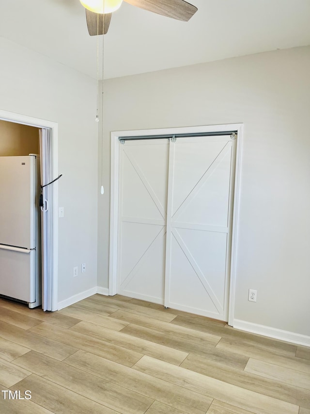 unfurnished bedroom featuring freestanding refrigerator, light wood-style flooring, baseboards, a ceiling fan, and a closet