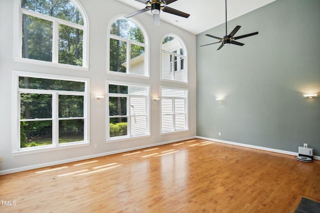 unfurnished living room with high vaulted ceiling, ceiling fan, baseboards, and wood finished floors