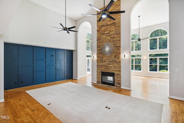 unfurnished living room featuring ceiling fan, high vaulted ceiling, arched walkways, wood finished floors, and a fireplace