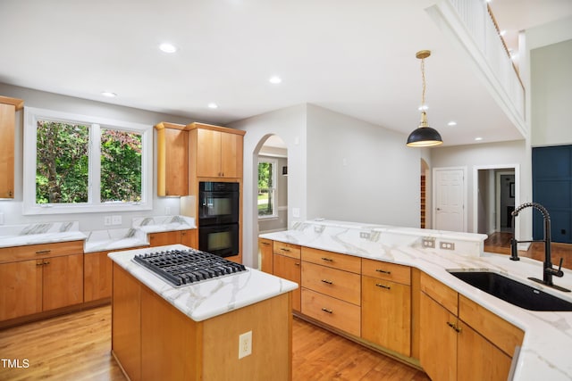 kitchen with a sink, stainless steel gas cooktop, arched walkways, light wood-style floors, and light stone counters