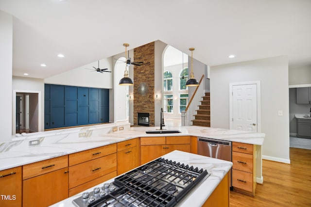kitchen with a sink, stainless steel appliances, light stone counters, ceiling fan, and light wood-style flooring