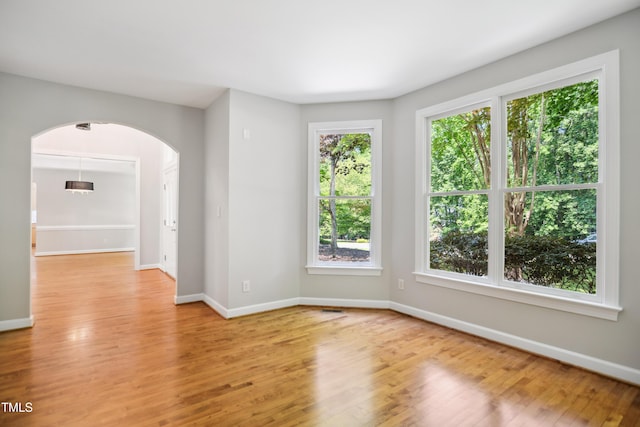 unfurnished room featuring arched walkways, light wood finished floors, and baseboards