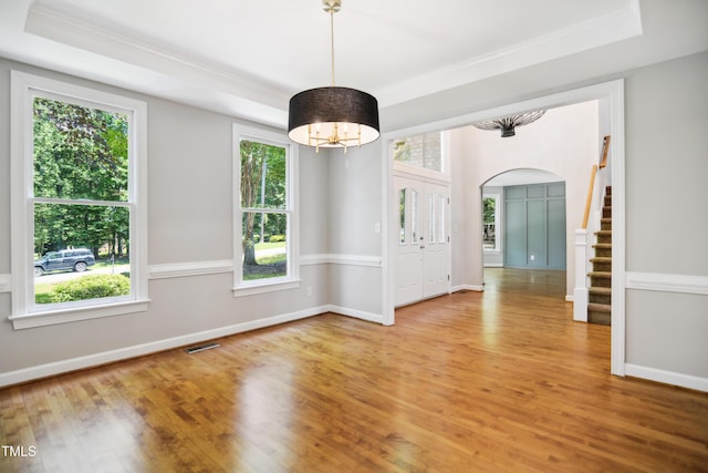 spare room with crown molding, healthy amount of natural light, arched walkways, and wood finished floors