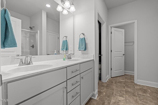 bathroom featuring a shower stall, double vanity, stone finish floors, and baseboards