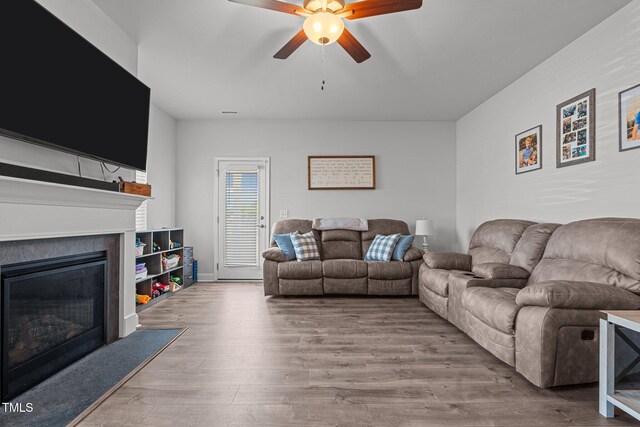 living area featuring a ceiling fan, a glass covered fireplace, and wood finished floors