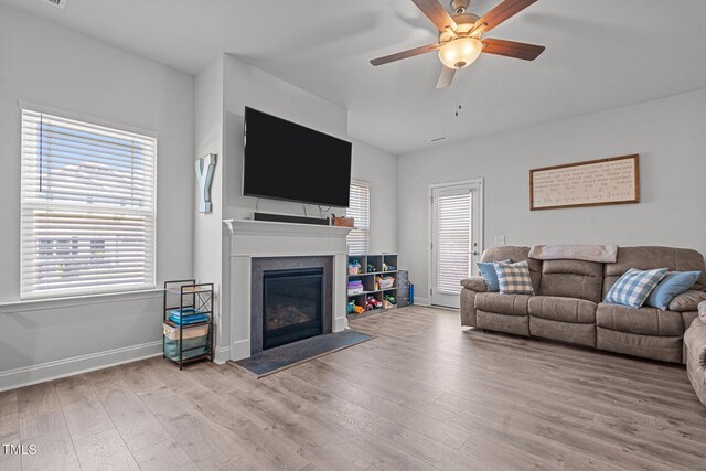 living room with wood finished floors, a ceiling fan, a glass covered fireplace, and baseboards