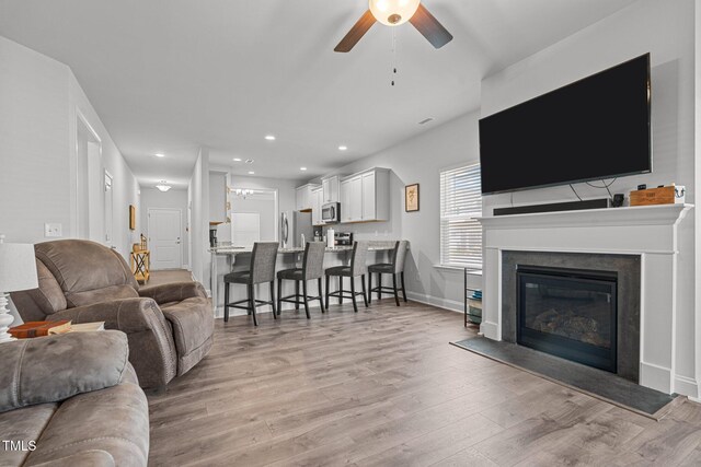 living area with ceiling fan, light wood finished floors, recessed lighting, baseboards, and a glass covered fireplace