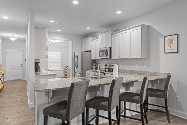 kitchen featuring appliances with stainless steel finishes, a peninsula, light stone counters, recessed lighting, and light wood-style floors