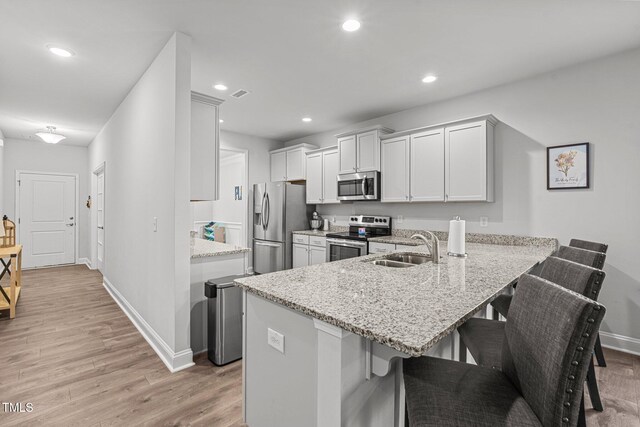 kitchen featuring appliances with stainless steel finishes, a breakfast bar area, a peninsula, baseboards, and a sink
