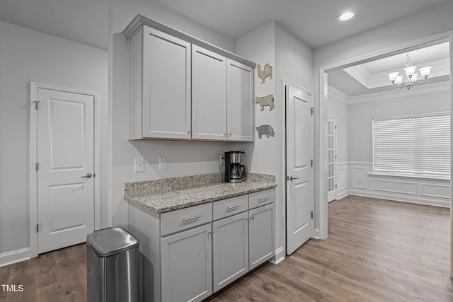 kitchen with a tray ceiling, ornamental molding, wood finished floors, a chandelier, and recessed lighting