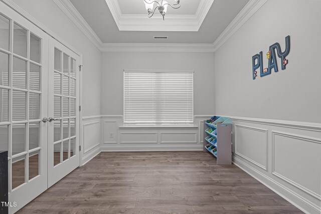 spare room featuring a tray ceiling, a chandelier, wood finished floors, wainscoting, and french doors