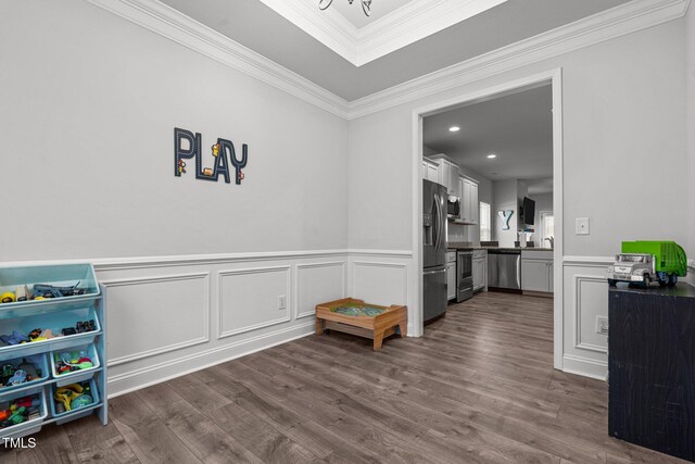 recreation room featuring dark wood finished floors, ornamental molding, wainscoting, a chandelier, and a decorative wall