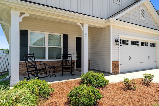 entrance to property with covered porch, stone siding, a garage, and driveway