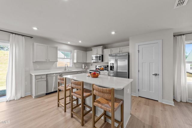 kitchen featuring stainless steel appliances, light wood-type flooring, a sink, a kitchen bar, and recessed lighting