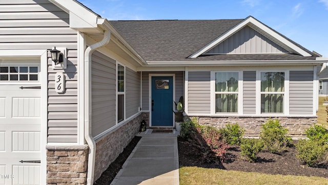 entrance to property with stone siding, an attached garage, a shingled roof, and board and batten siding