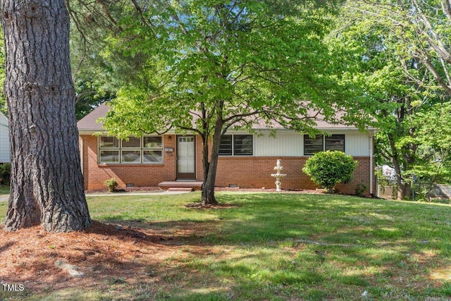 view of property hidden behind natural elements with brick siding, a front lawn, and crawl space