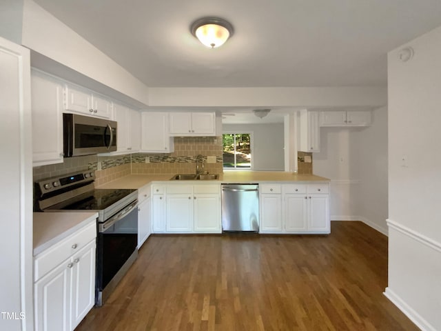 kitchen with appliances with stainless steel finishes, a sink, backsplash, and dark wood-type flooring