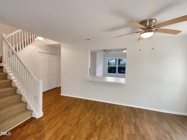unfurnished living room featuring wood finished floors, baseboards, a ceiling fan, and stairway