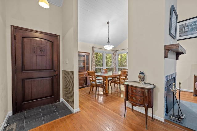 entryway with wood finished floors, a tile fireplace, and vaulted ceiling