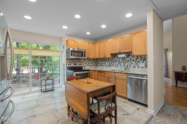 kitchen featuring appliances with stainless steel finishes, a sink, decorative backsplash, light stone finish flooring, and light brown cabinetry