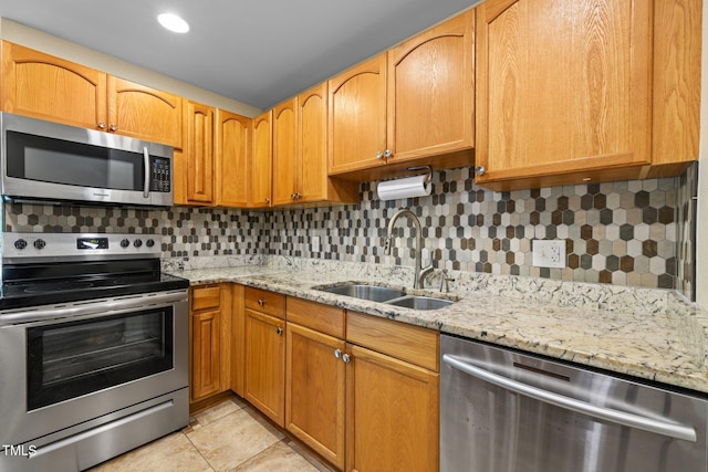 kitchen with stainless steel appliances, a sink, tasteful backsplash, and light stone countertops