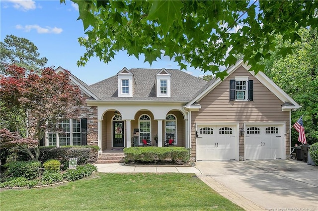 traditional home featuring concrete driveway, a front yard, roof with shingles, a porch, and stone siding