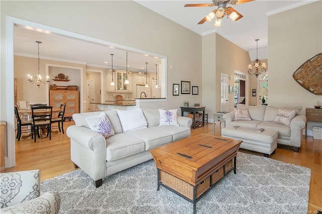 living room featuring a chandelier, a ceiling fan, light wood-style floors, and ornamental molding