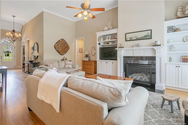 living room featuring ornamental molding, light wood-style floors, a chandelier, a fireplace with flush hearth, and ceiling fan