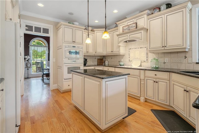 kitchen featuring cream cabinets, light wood-style floors, a center island, tasteful backsplash, and ornamental molding