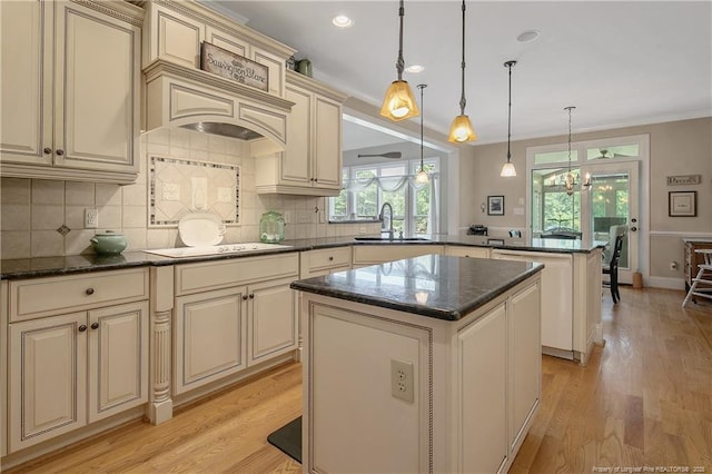kitchen with cream cabinets, a peninsula, a sink, white electric stovetop, and a center island