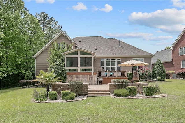 back of house featuring a sunroom, a wooden deck, a lawn, and a shingled roof