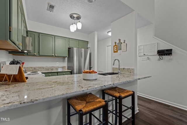 kitchen with green cabinetry, a sink, freestanding refrigerator, a peninsula, and light stone countertops