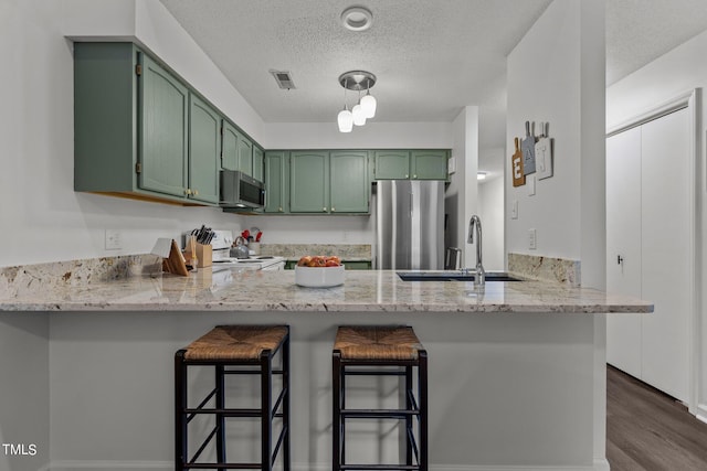 kitchen with green cabinets, a peninsula, appliances with stainless steel finishes, and a textured ceiling