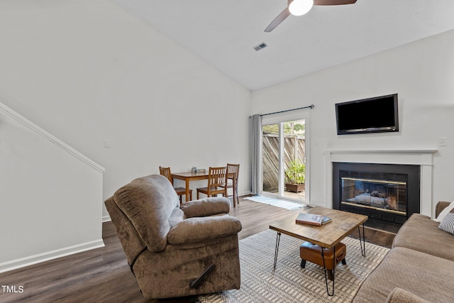 living area with wood finished floors, ceiling fan, a glass covered fireplace, high vaulted ceiling, and baseboards