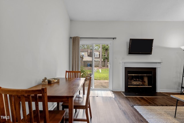 dining space with dark wood-type flooring, a fireplace with flush hearth, and baseboards