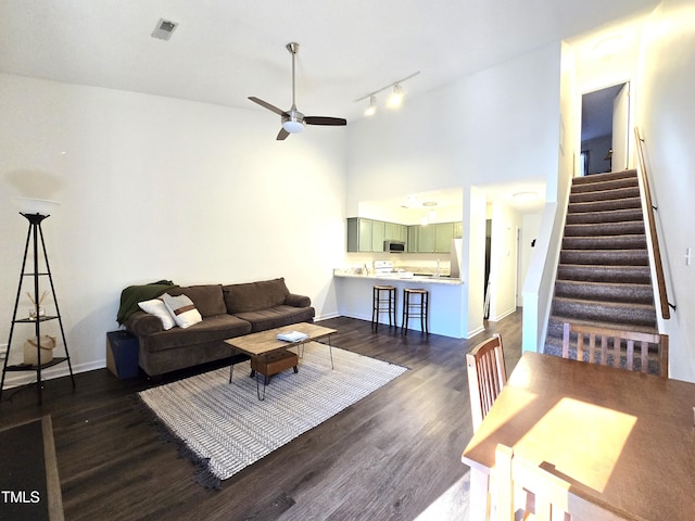 living room with a ceiling fan, dark wood-style flooring, stairway, baseboards, and a towering ceiling