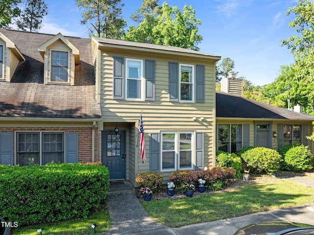 view of front of home featuring a chimney, a shingled roof, and a front yard