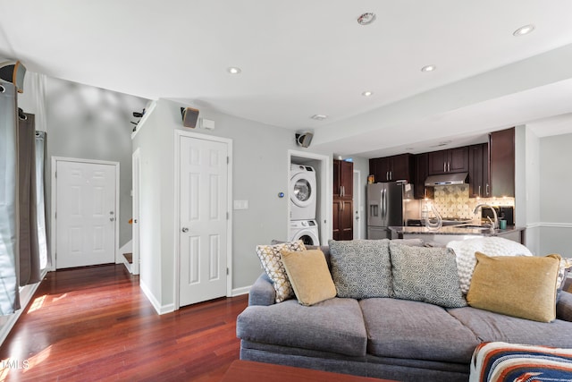 living room featuring stacked washer / drying machine, dark wood finished floors, recessed lighting, and baseboards