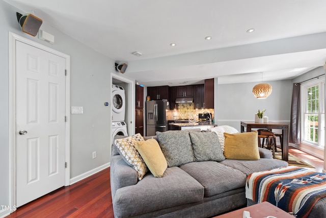 living room featuring stacked washer / dryer, dark wood finished floors, recessed lighting, and baseboards
