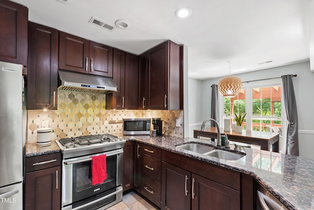 kitchen with stainless steel appliances, under cabinet range hood, a sink, tasteful backsplash, and dark stone counters