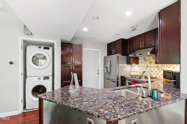 kitchen with stacked washer and clothes dryer, under cabinet range hood, stainless steel fridge with ice dispenser, dark stone countertops, and dark wood-type flooring