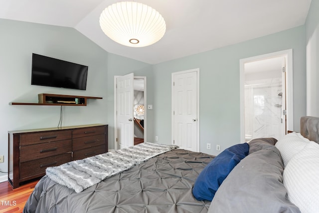 bedroom with vaulted ceiling, light wood-style floors, and connected bathroom