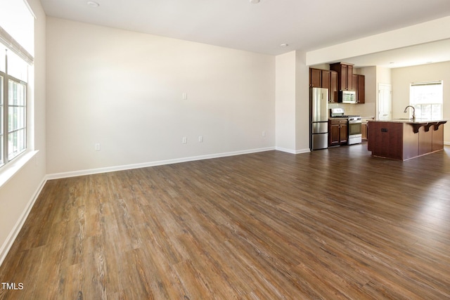 unfurnished living room featuring a sink, dark wood-style floors, and baseboards