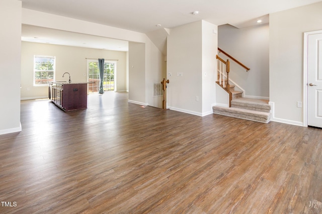 unfurnished living room with a sink, dark wood-style floors, stairway, and baseboards