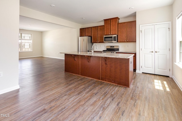 kitchen featuring appliances with stainless steel finishes, wood finished floors, a center island with sink, a sink, and a kitchen breakfast bar