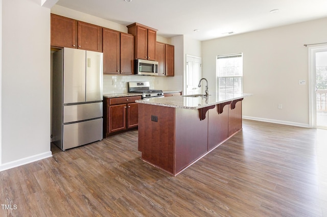 kitchen with stainless steel appliances, a sink, dark wood-style floors, decorative backsplash, and an island with sink