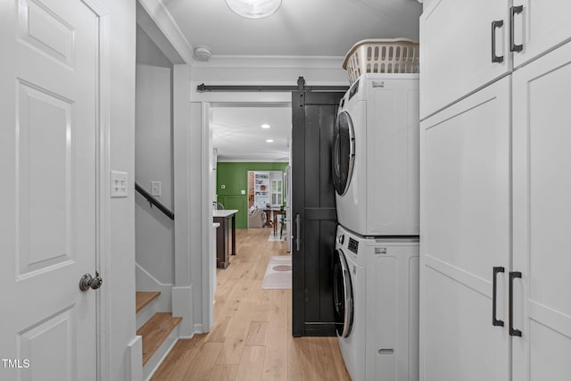 laundry area featuring stacked washer / drying machine, light wood-style flooring, ornamental molding, cabinet space, and recessed lighting