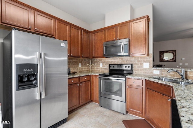 kitchen with appliances with stainless steel finishes, a sink, brown cabinetry, and tasteful backsplash