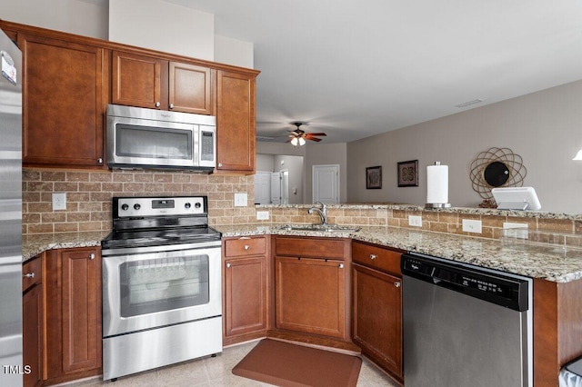 kitchen with stainless steel appliances, a sink, a peninsula, brown cabinets, and backsplash